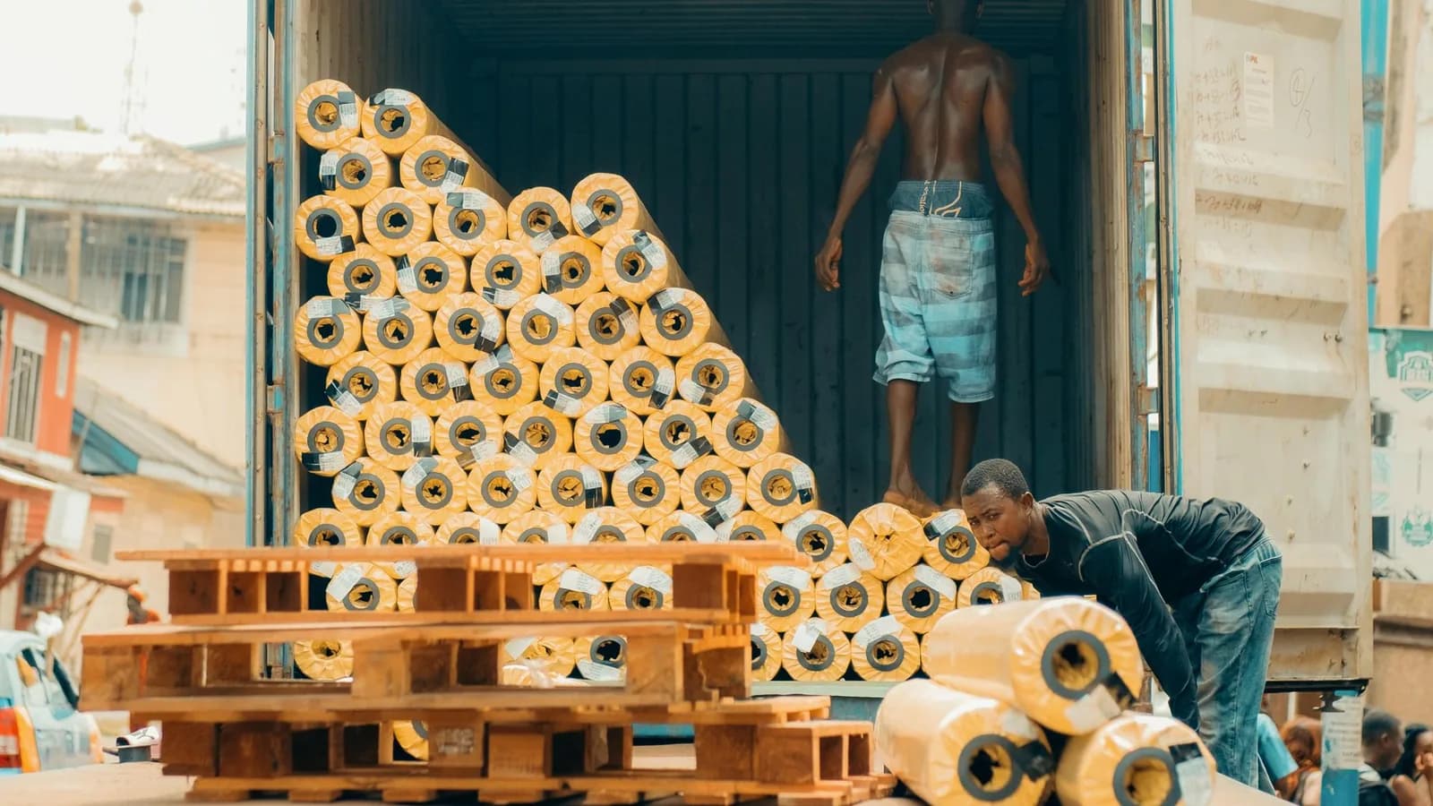 Workers loading rolls of fabric into a shipping container in Kumasi