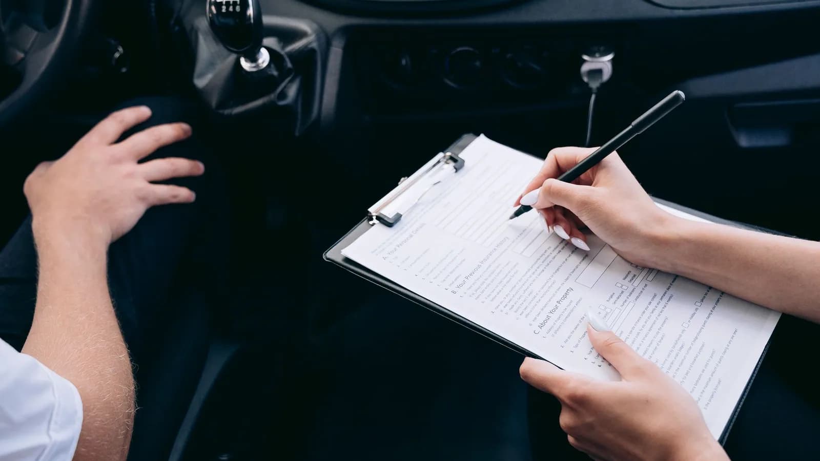 Hands completing a claim form on a clipboard inside a car